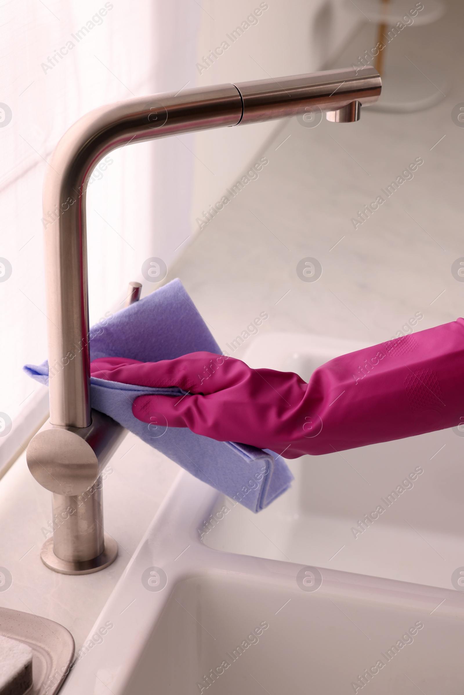 Photo of Woman in gloves cleaning faucet of kitchen sink with rag, closeup