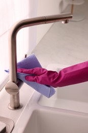 Woman in gloves cleaning faucet of kitchen sink with rag, closeup