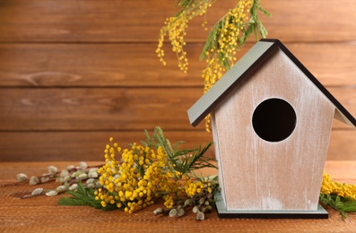 Stylish bird house and fresh flowers on wooden table. Space for text