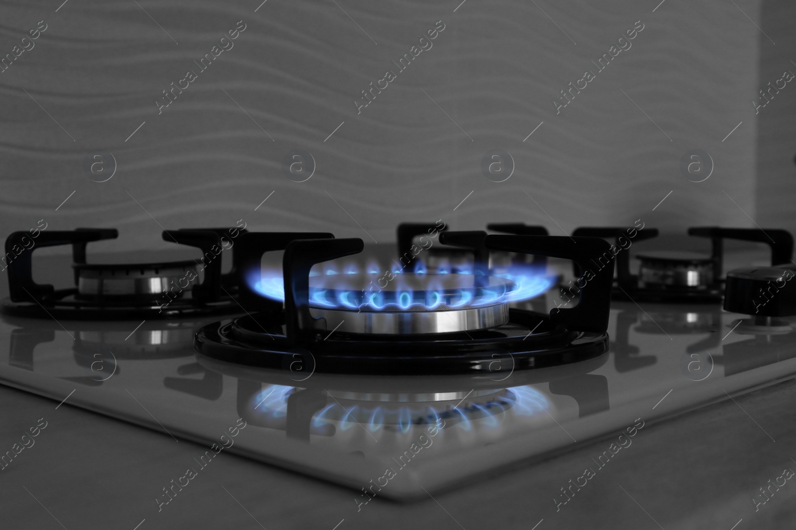 Photo of Modern gas cooktop with burning blue flame in kitchen