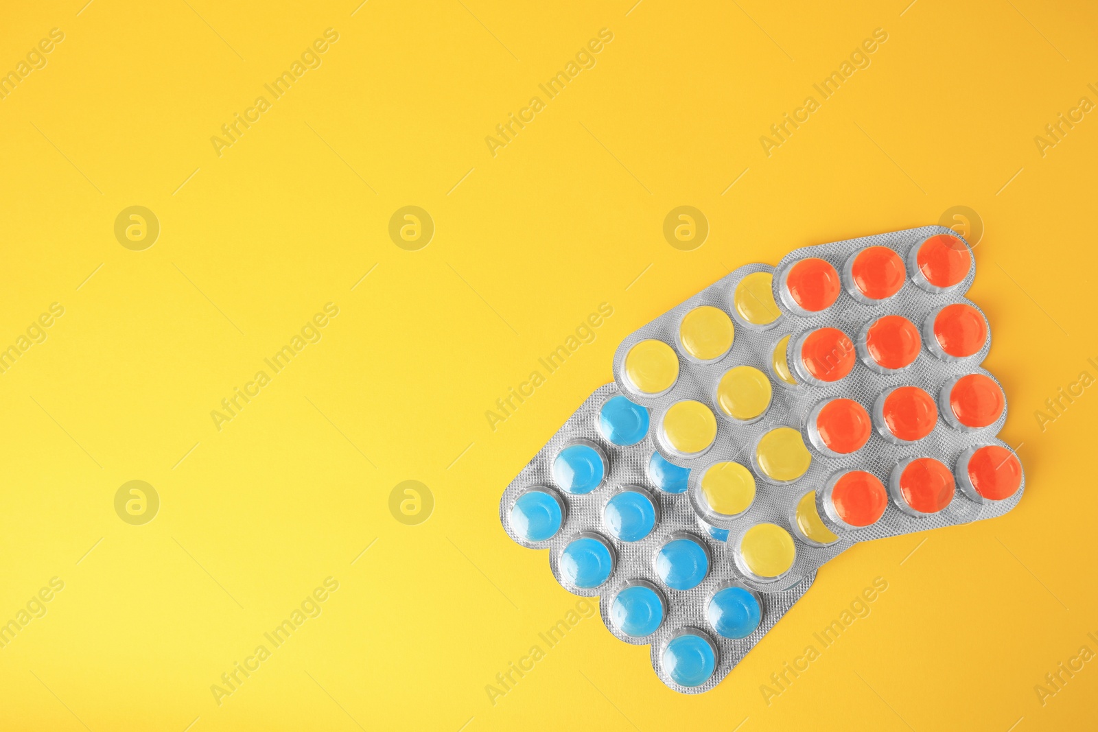 Photo of Blisters with cough drops on yellow background, flat lay. Space for text