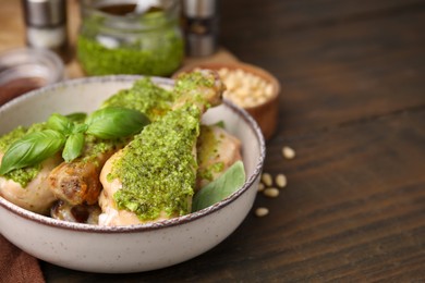 Photo of Delicious fried chicken drumsticks with pesto sauce and basil in bowl on wooden table. Space for text