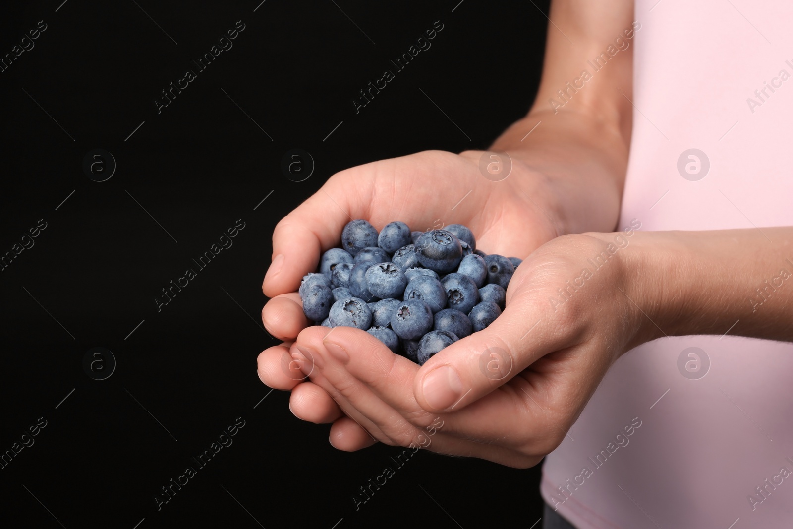 Photo of Woman holding juicy fresh blueberries on black background, closeup