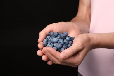 Woman holding juicy fresh blueberries on black background, closeup