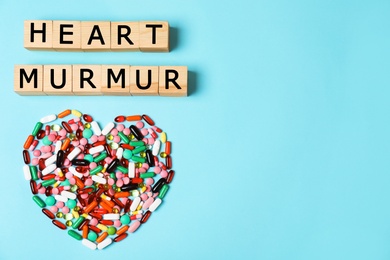 Photo of Heart made of pills and wooden cubes on color background, top view with space for text. Cardiology concept