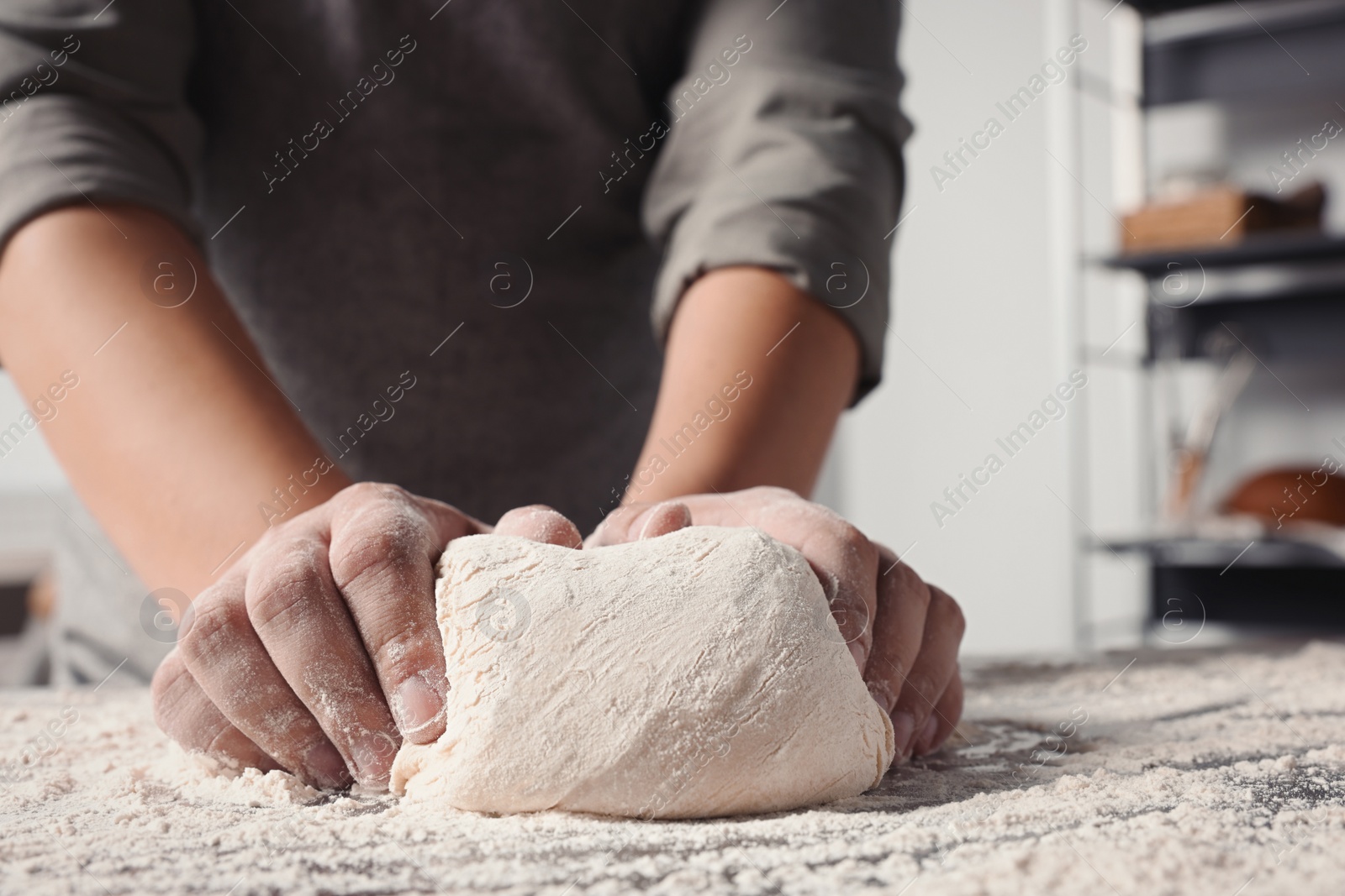 Photo of Man kneading dough at table in kitchen, closeup