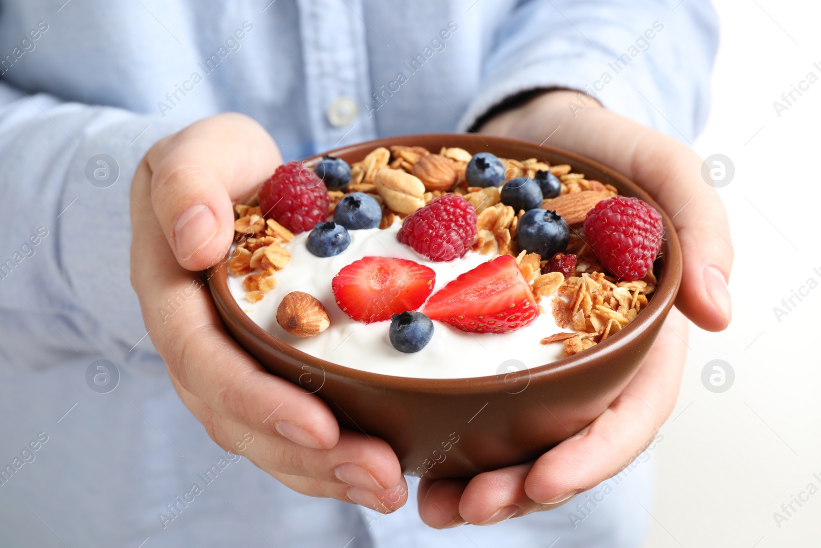 Photo of Woman holding tasty homemade granola with yogurt and berries in bowl, closeup. Healthy breakfast
