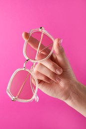 Photo of Woman holding stylish sunglasses on pink background, closeup of hand