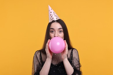 Woman in party hat inflating balloon on orange background