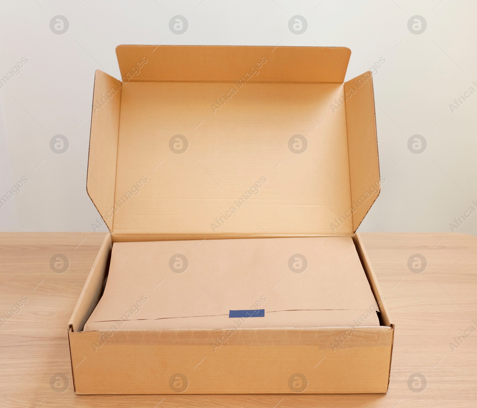 Photo of Open cardboard box with item wrapped in kraft paper on wooden table. Delivery service