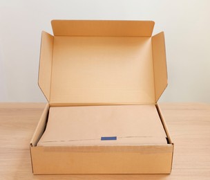 Open cardboard box with item wrapped in kraft paper on wooden table. Delivery service