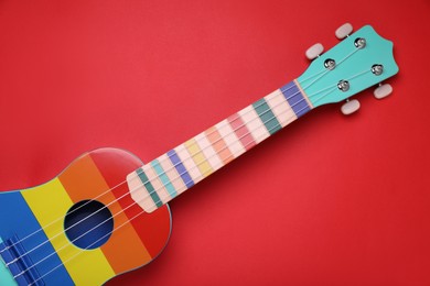 Colorful ukulele on red background, top view. String musical instrument