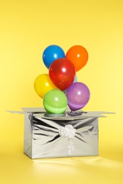 Gift box with bright air balloons on color background