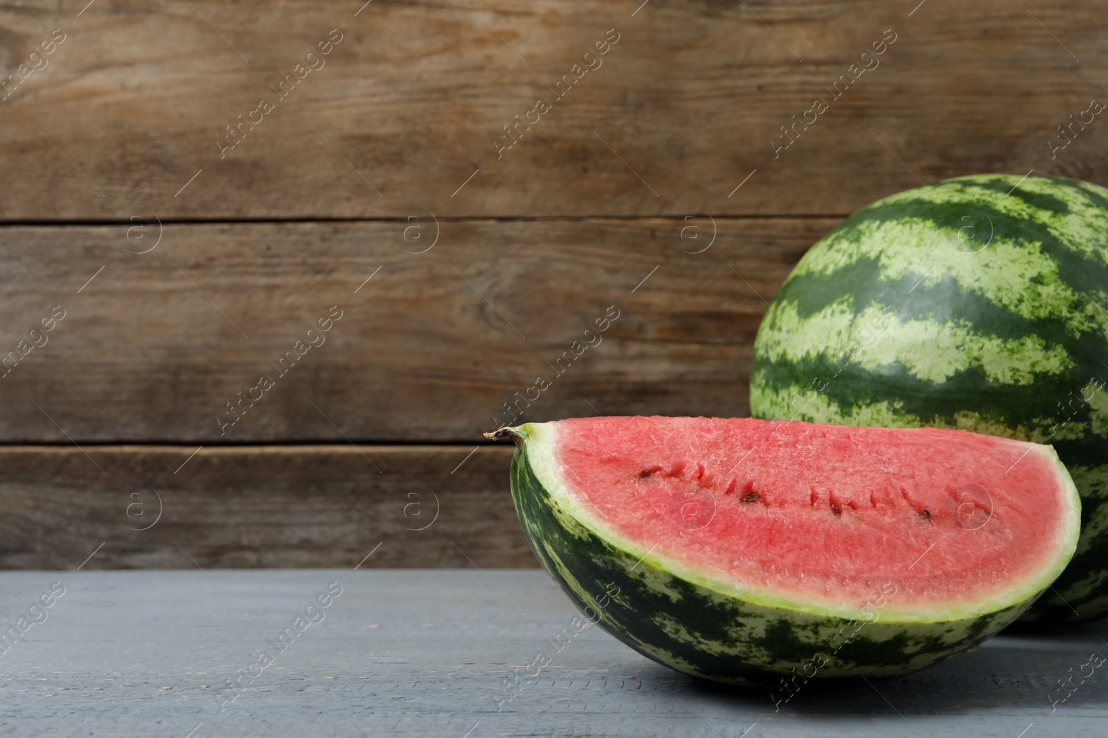 Photo of Tasty whole and cut watermelons on grey wooden table. Space for text