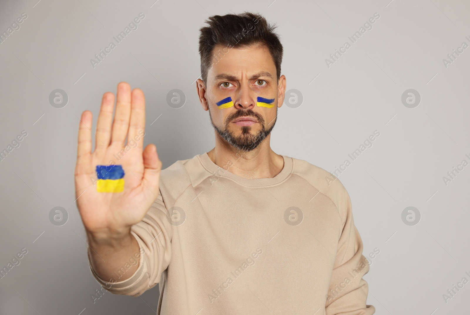 Photo of Angry man with drawings of Ukrainian flag on face and palm against light grey background