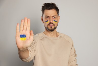 Photo of Angry man with drawings of Ukrainian flag on face and palm against light grey background