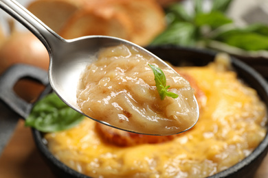 Photo of Spoon with fresh homemade french onion soup over bowl, closeup