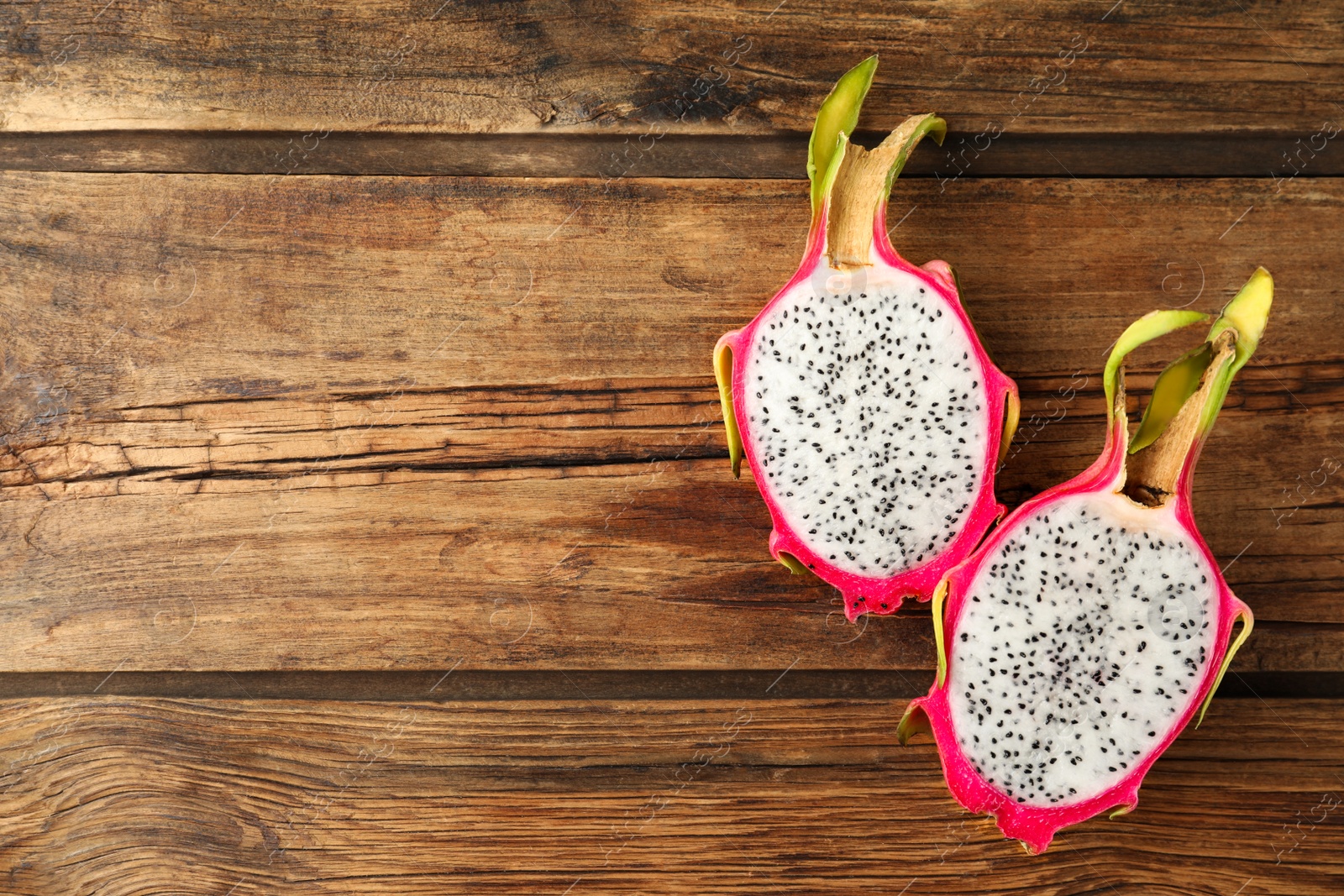 Photo of Halves of delicious ripe dragon fruit (pitahaya) on wooden table, flat lay. Space for text