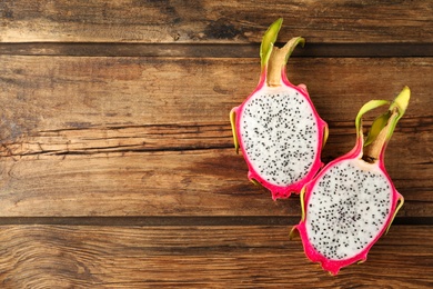 Halves of delicious ripe dragon fruit (pitahaya) on wooden table, flat lay. Space for text