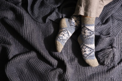 Woman wearing knitted socks on warm plaid, top view. Cozy season
