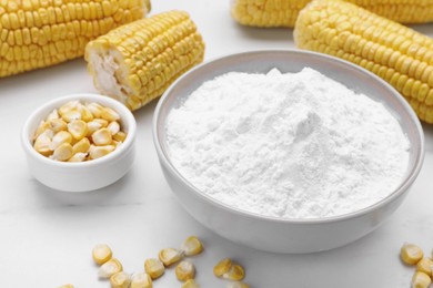 Photo of Bowl with corn starch, ripe cobs and kernels on white table, closeup