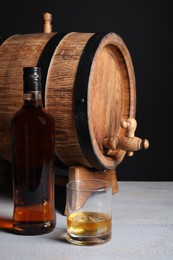 Barrel with tap, bottle and glass of tasty whiskey on light gray wooden table