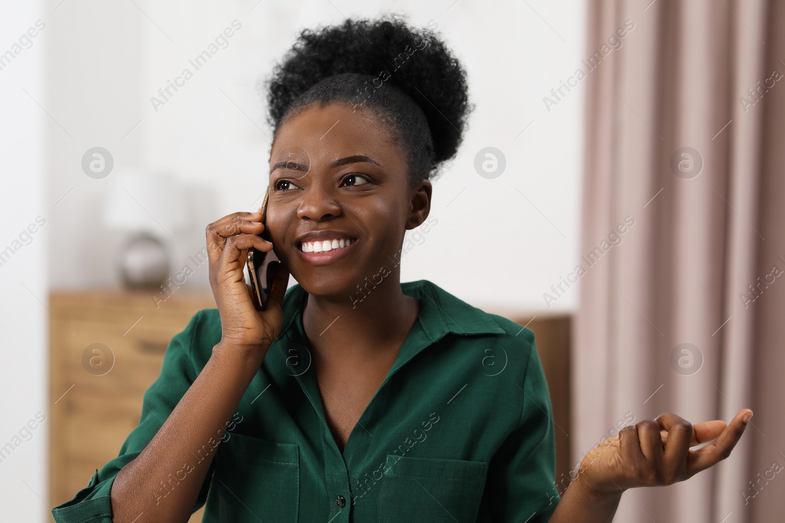 Photo of Happy young woman talking on smartphone at home