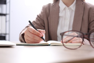 Photo of Woman writing in notebook at wooden table in office, closeup