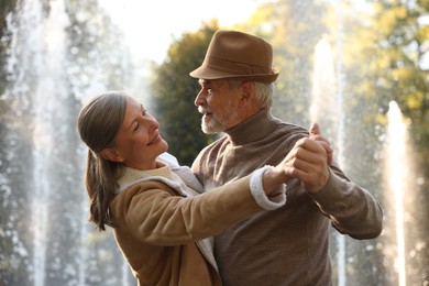 Photo of Affectionate senior couple dancing together near fountain outdoors. Romantic date