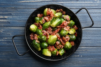 Photo of Tasty roasted Brussels sprouts with bacon on blue wooden table, top view