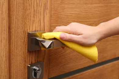 Woman cleaning door handle with rag indoors, closeup