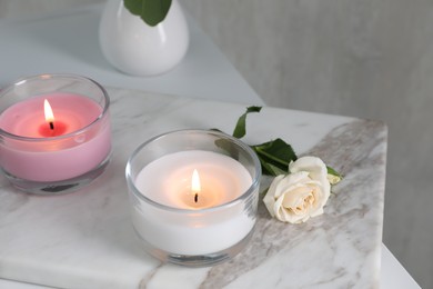Photo of Burning candles and beautiful rose on white marble board
