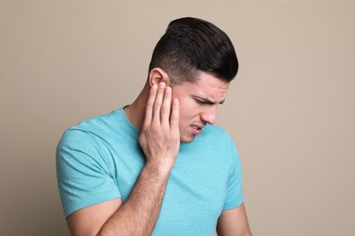 Photo of Man suffering from ear pain on beige background