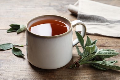 Cup of aromatic sage tea and fresh leaves on wooden table