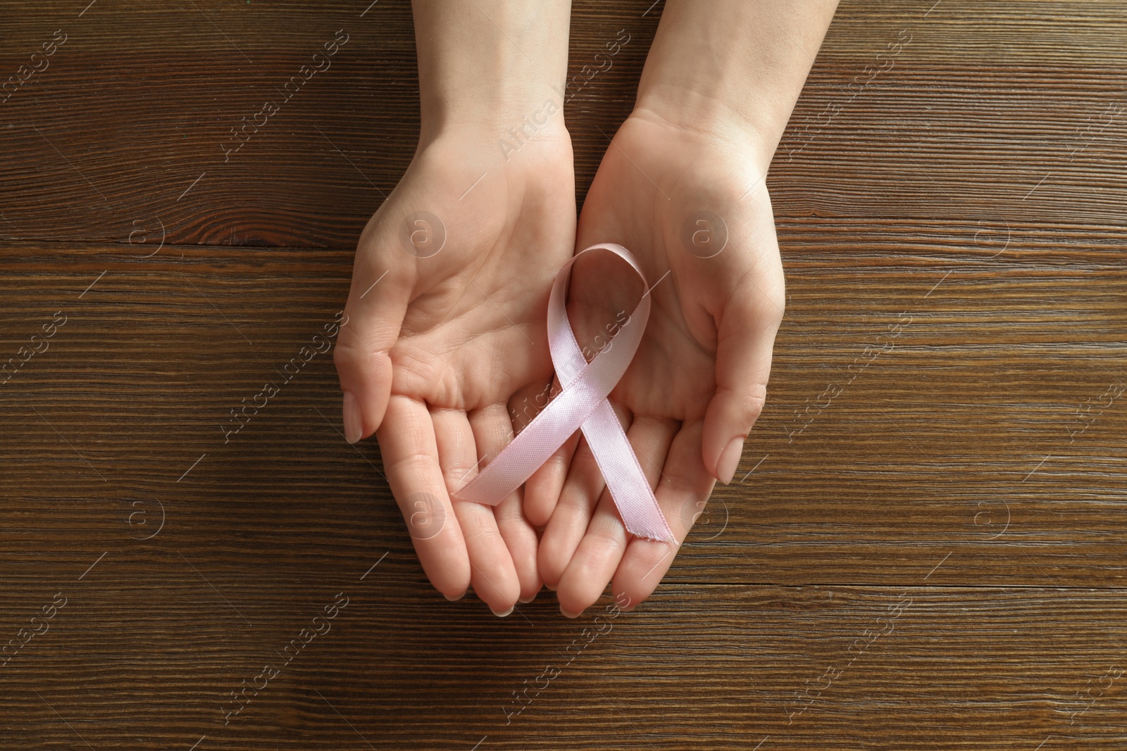 Photo of Woman holding pink ribbon on wooden background, top view. Breast cancer awareness