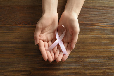 Woman holding pink ribbon on wooden background, top view. Breast cancer awareness