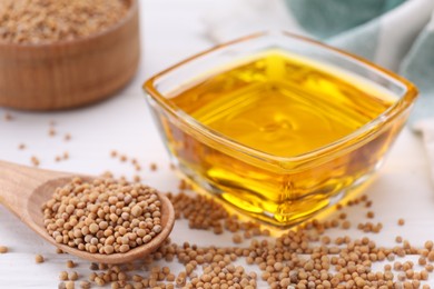 Photo of Bowl of natural oil and mustard seeds on white table, closeup