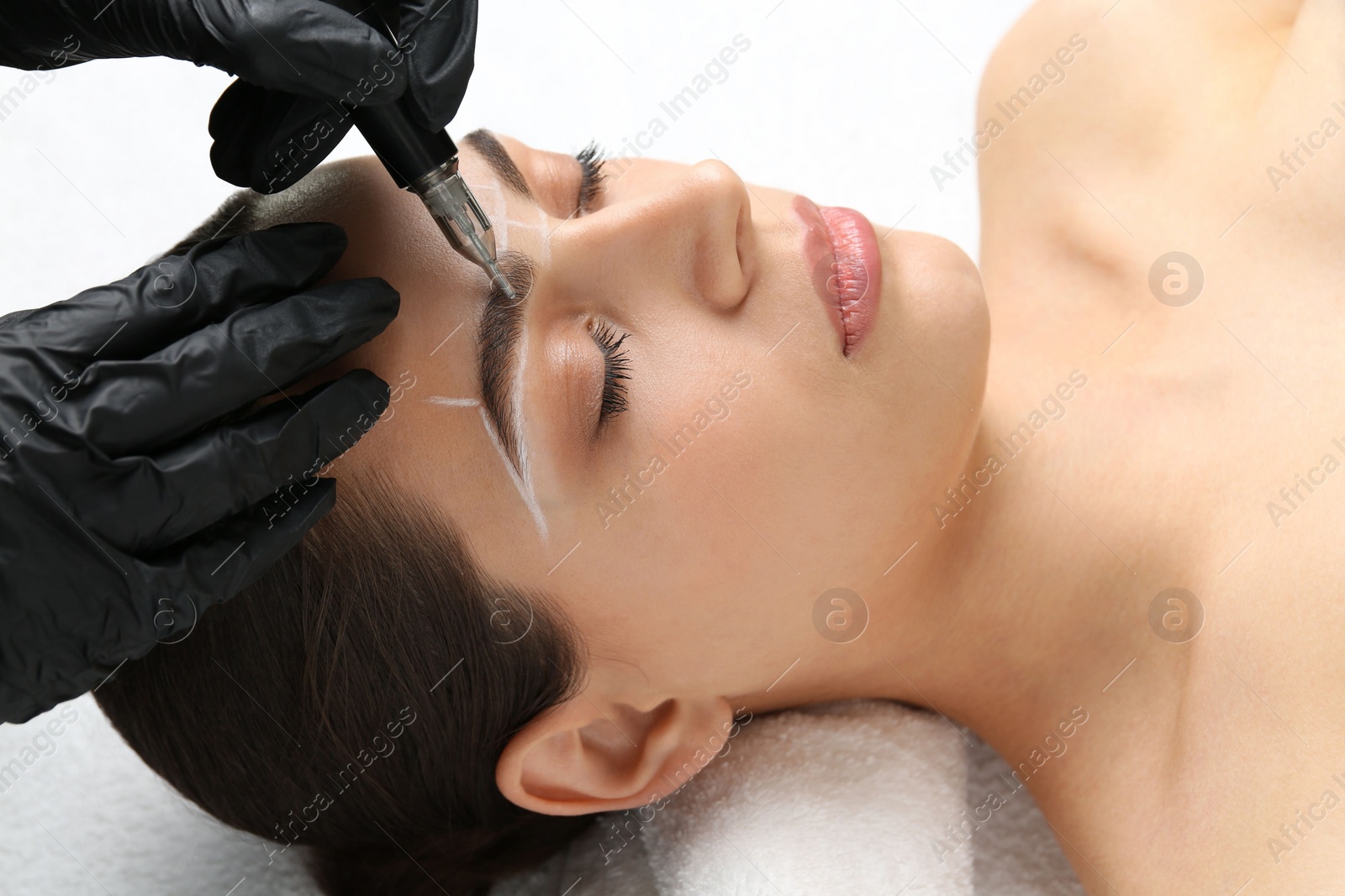 Photo of Beautician making permanent eyebrow makeup to young woman on white background, closeup