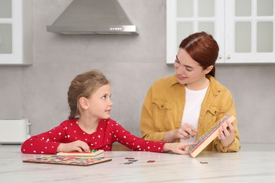 Photo of Happy mother and daughter playing with different colorful cubes and equations at white marble table in kitchen. Learning mathematics with fun