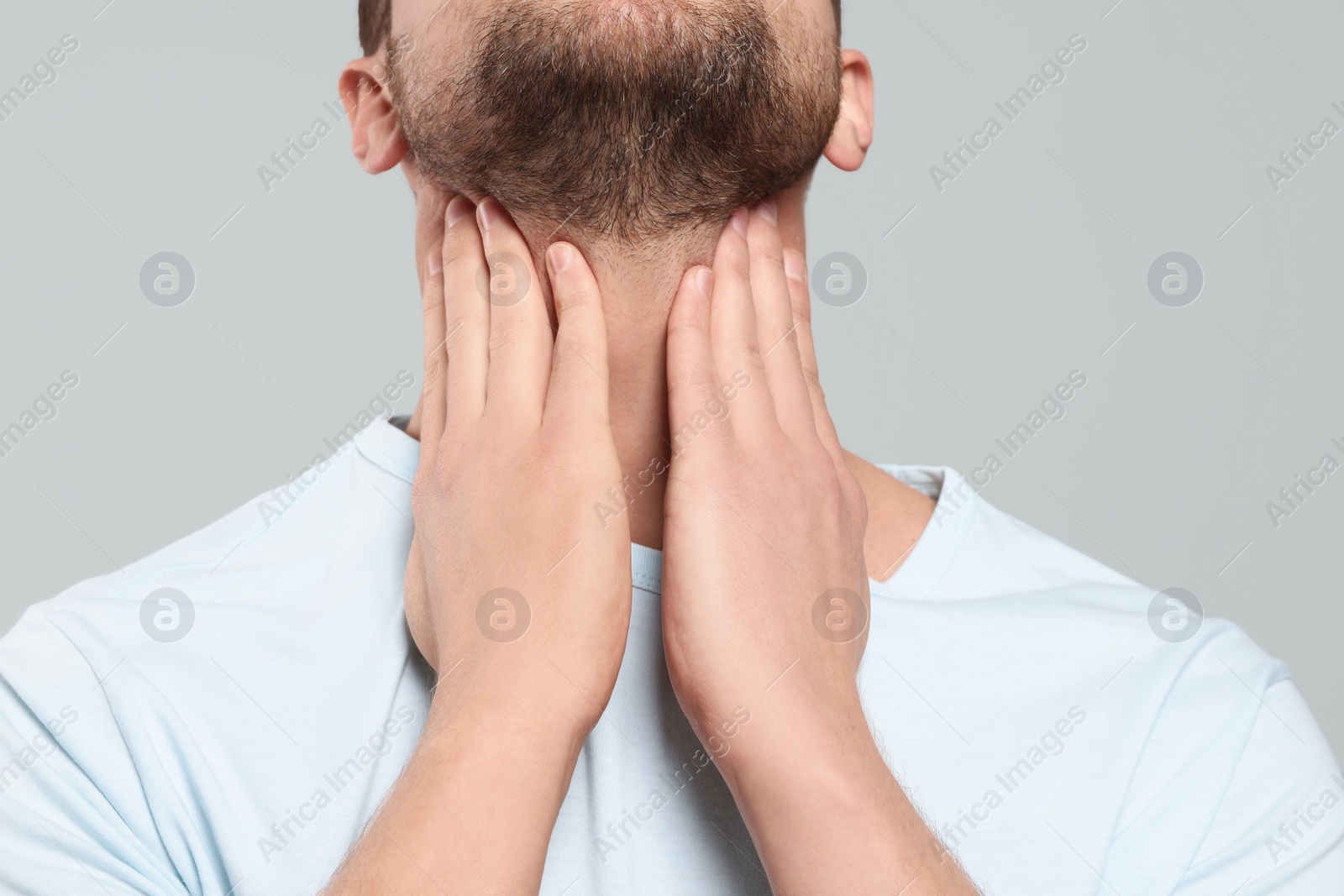 Photo of Man suffering from sore throat on light gray background, closeup