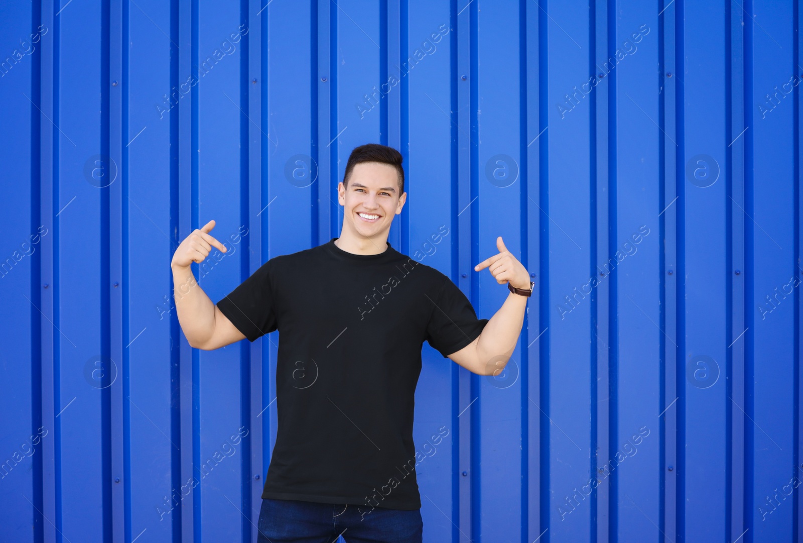 Photo of Young man in black t-shirt near color wall. Mockup for design