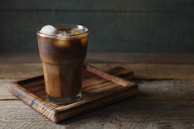 Photo of Glass of delicious iced coffee with milk on wooden table, space for text
