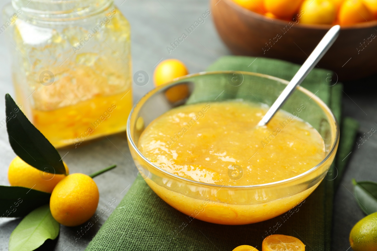 Photo of Delicious kumquat jam in bowl and fresh fruits on grey table, closeup