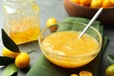 Photo of Delicious kumquat jam in bowl and fresh fruits on grey table, closeup