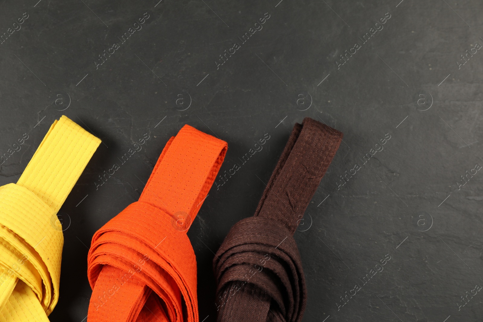 Photo of Colorful karate belts on gray background, flat lay. Space for text