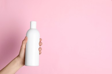 Woman holding shampoo bottle on pink background, top view. Space for text