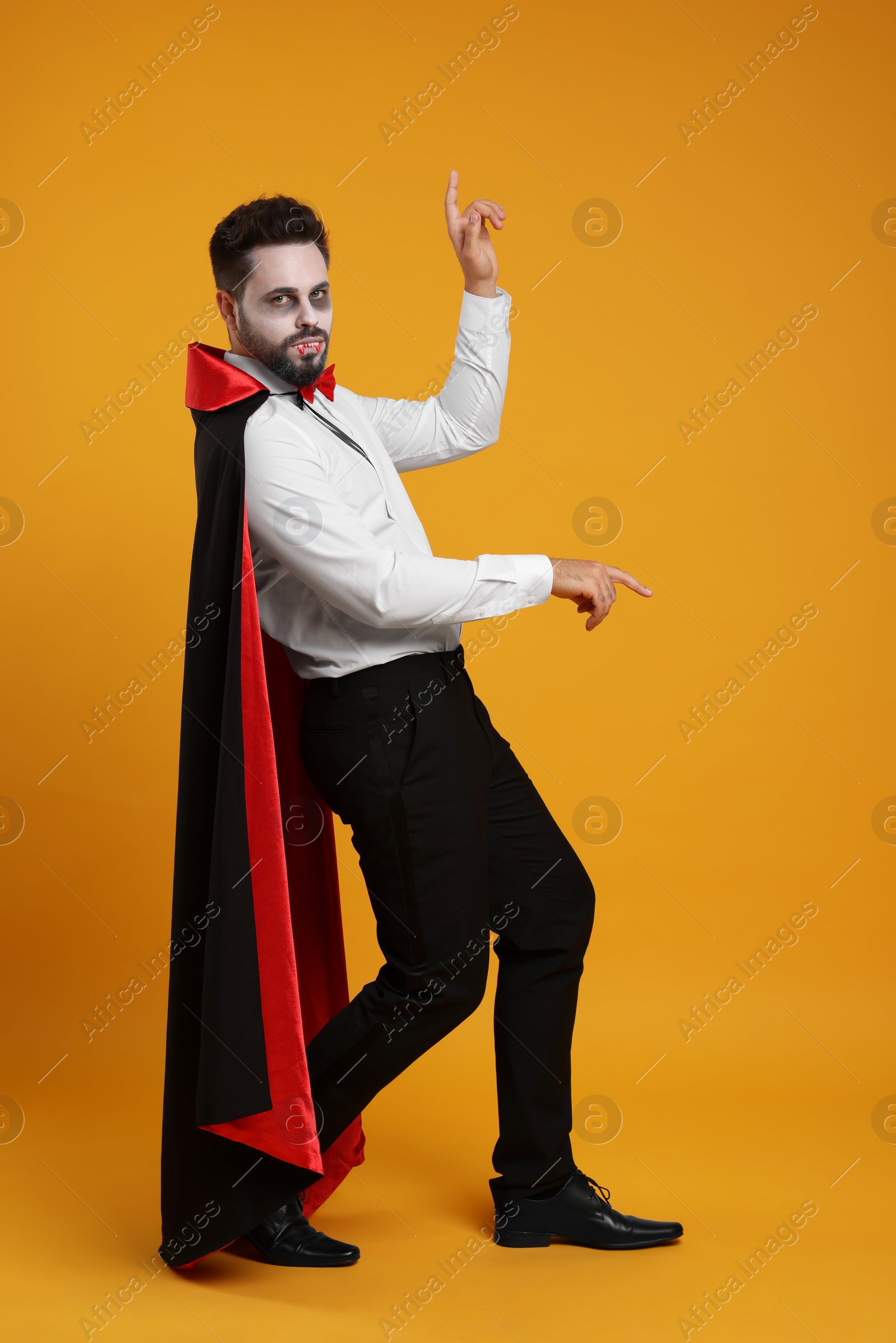 Photo of Man in scary vampire costume with fangs posing on orange background. Halloween celebration