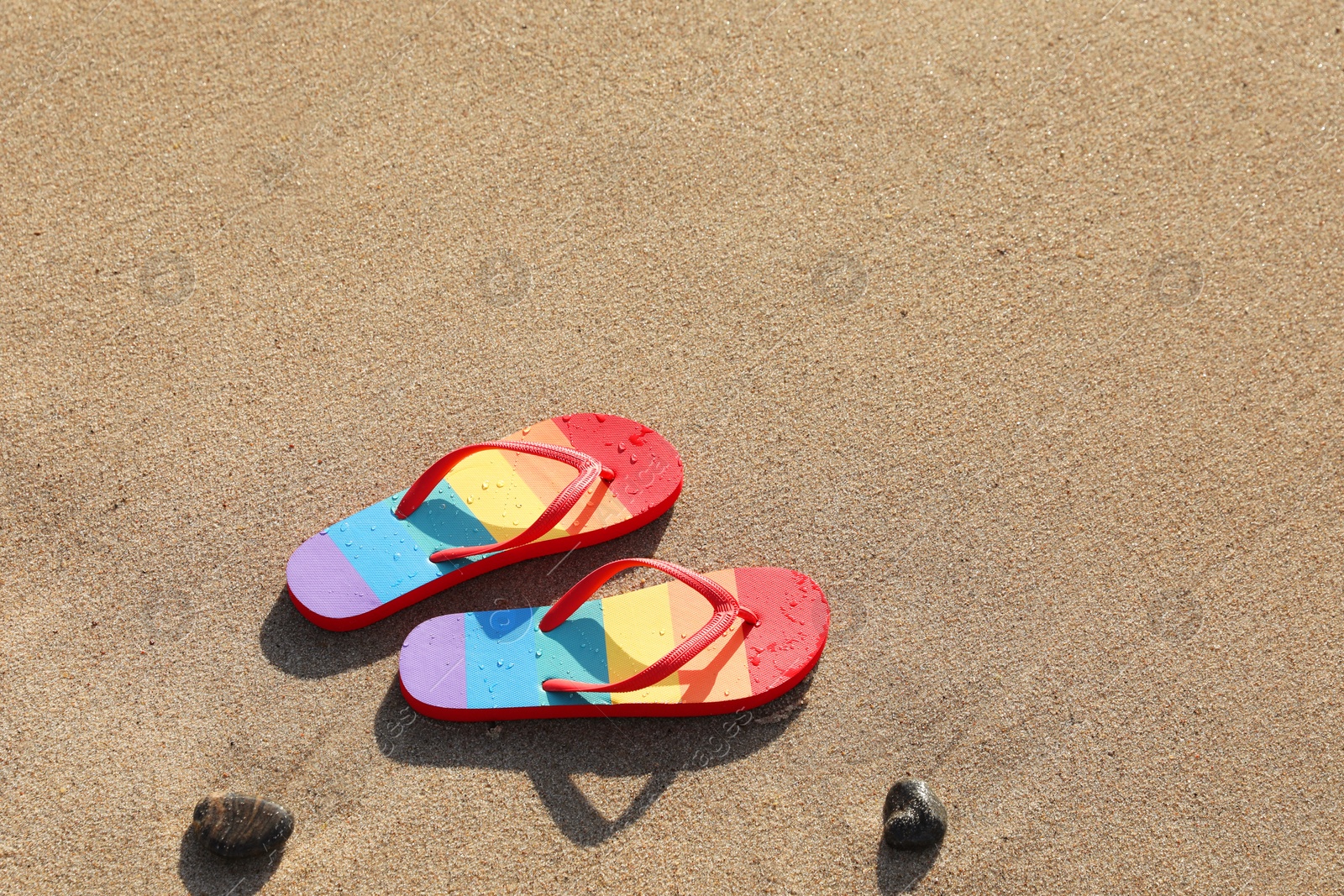 Photo of Stylish rainbow flip flops on sand at beach, above view. Space for text