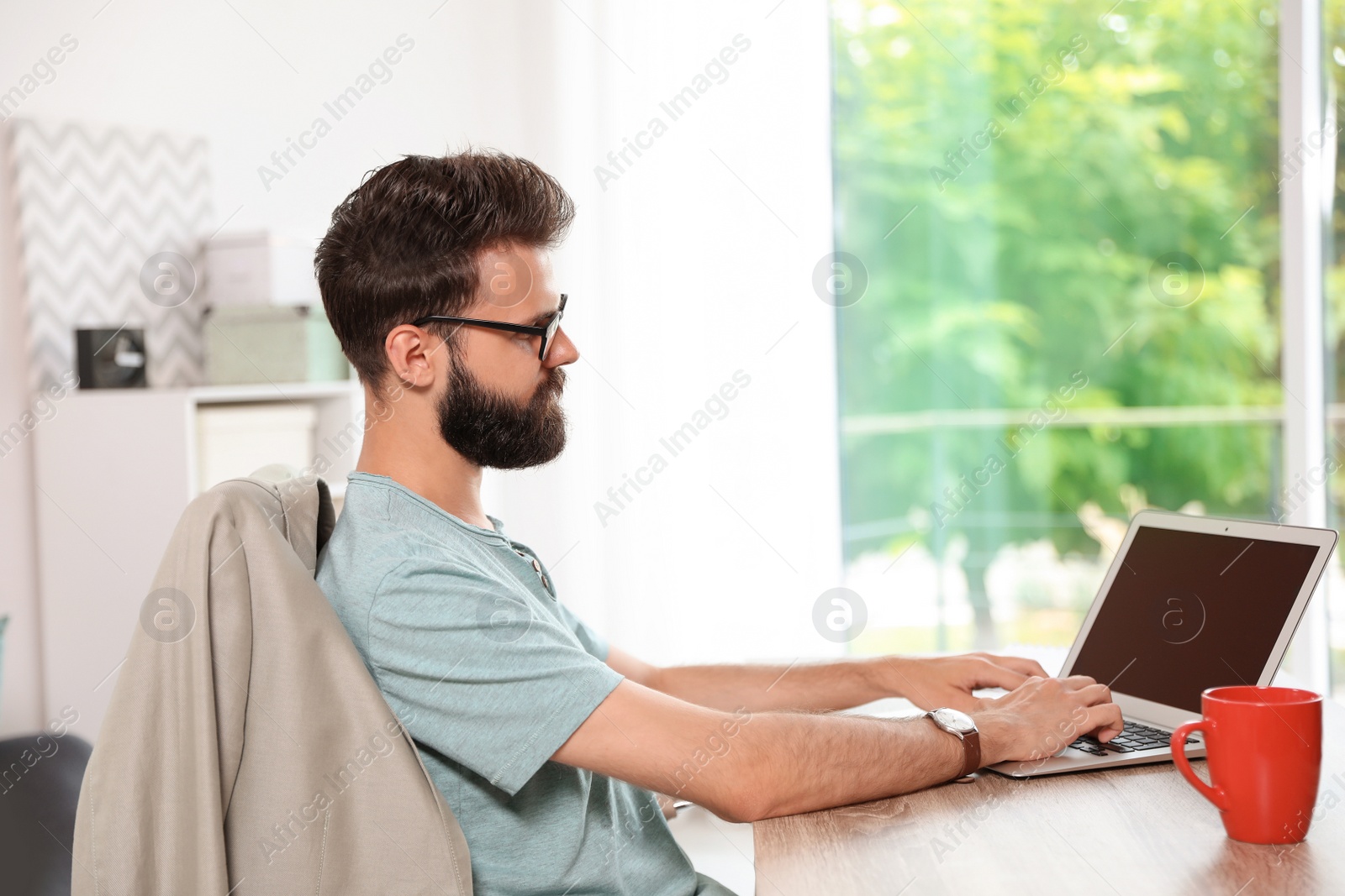 Photo of Young bearded man working with laptop at home