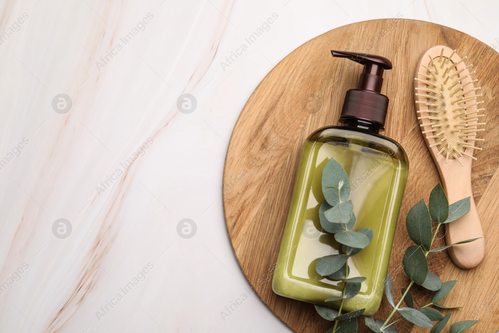 Photo of Shampoo bottle, hair brush and green leaves on white marble table, top view. Space for text